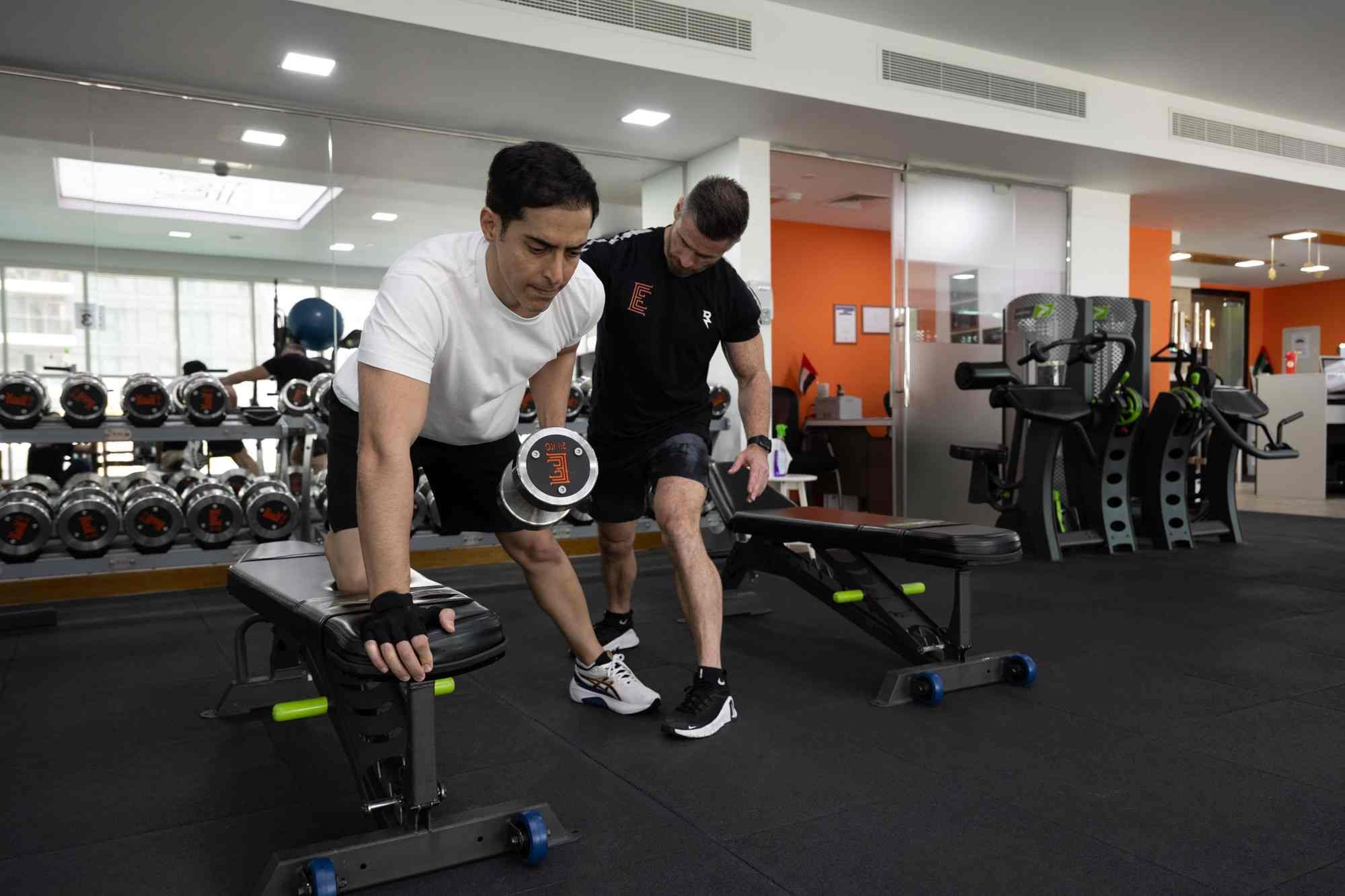 An Elite Fitness client performing a dumbbell exercise with coaching