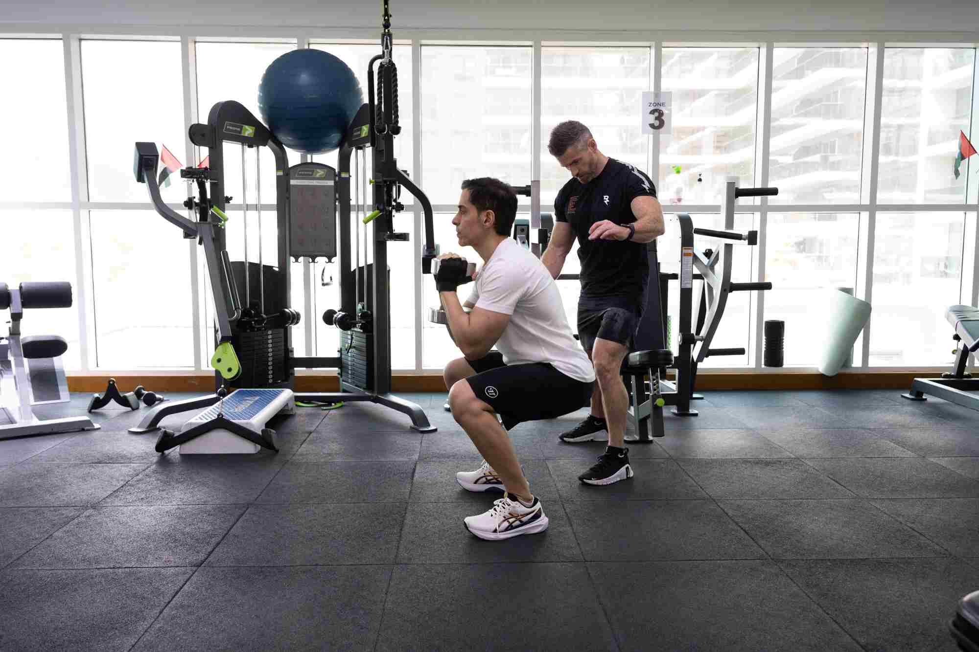 An Elite Fitness coach guiding a client through a squat